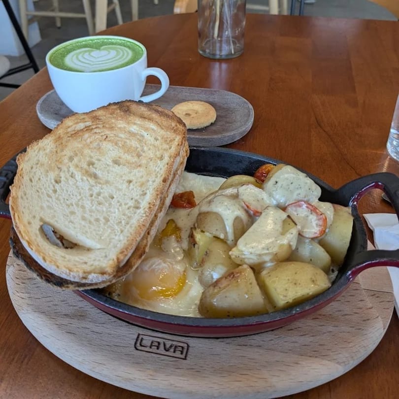 Queen B's breakfast skillet with eggs, potatoes, and toast, alongside a green matcha latte.