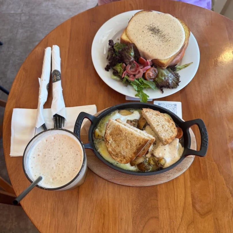 A Queen B coffee and two breakfast dishes, one with toast and salad, the other in a skillet.