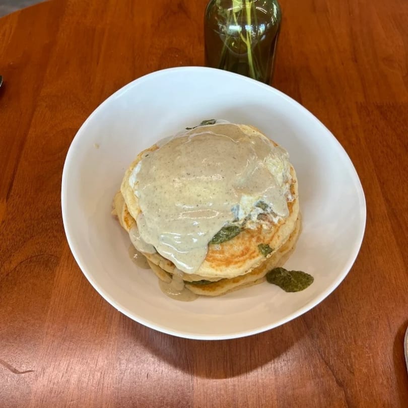 Stack of pancakes topped with a light-colored sauce and green garnish in a white bowl.